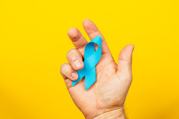 Male hand holding blue ribbon symbolizing awareness for cancer prevention