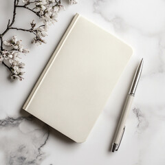 Minimalist white notebook with a silver pen on a marble surface, accompanied by delicate blooming flowers, creating an elegant and inspiring workspace aesthetic