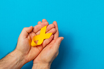 Hands holding a yellow ribbon symbolizing cancer awareness and support