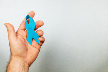 Hand holding a blue awareness ribbon symbolizing cancer support and prevention