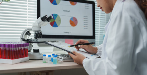 Scientist wearing lab coat analyzing medical report on clipboard with pen, blood test tubes and...