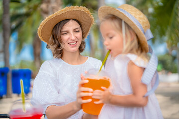 Relaxing day at the beach with mother and daughter enjoying refreshing drinks under palm trees