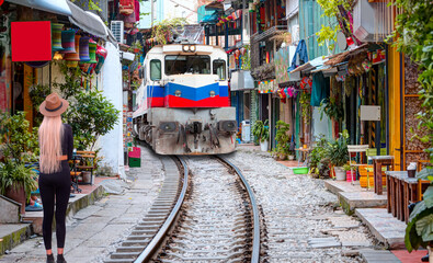 A beautiful woman in black tights and a beige hat is standing - Hanoi city railway perspective, The train runs through Phung Hung street coffee cafe, a famous place for tourists 