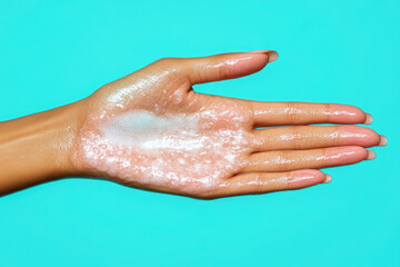 Fototapeta premium A hand covered in a Skincare, showcasing a vibrant teal background, suggests a focus on skincare or cleaning products.