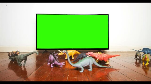 Plastic dinosaurs come to watch TV on an old wooden floor green screen, stop motion 
