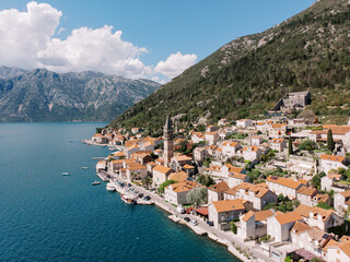 Perast promenade with ancient stone houses and a church bell tower at the foot of the mountains. Montenegro. Drone