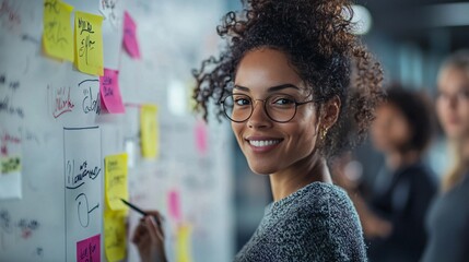 Woman with curly hair writing on sticky notes at modern office during collaborative brainstorming session