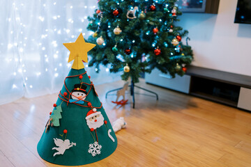 Decorated felt Christmas tree stands near a large Christmas tree in the room