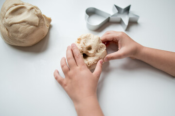 Child hands kneading dough with heart and star cookie cutters on white surface