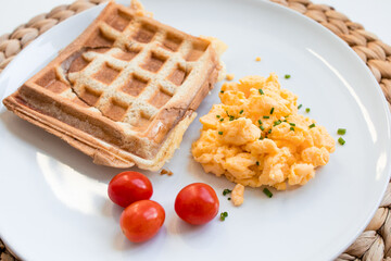 Breakfast plate with toast sandwich, scrambled eggs, and cherry tomatoes on white plate