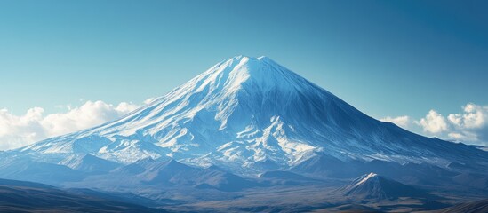 Majestic snow-covered mountain peak under a clear blue sky with soft white clouds surrounding the summit creating a serene landscape.