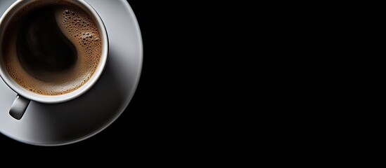 Top view of a coffee cup with dark brown beverage on a gray saucer against a solid black background ideal for text overlay or branding.