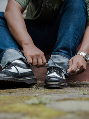 Detail of vintage wing-toed brogue shoes shining on a mossy block. Close-up view of a man tying black and white genuine leather brogue shoelaces outdoors.