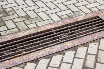 A rusty metal grate is currently sitting on a weathered brick sidewalk