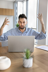 Annoyed man using laptop experiences problems with device, reading unpleasant business or personal...