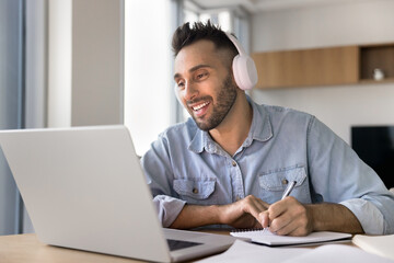 Obraz premium Smiling man studying online, wear wireless headphone engaged in webinar, gaining new professional knowledge, listening audio course, develop foreign languages skills. Education using modern technology