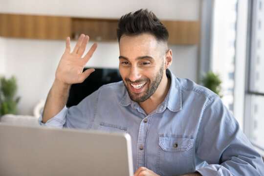 Hispanic man start videocall seated at desk looking at laptop screen enjoy remote digital communication, participate in job interview, personal chat or conversation with family using videoconference