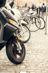 Obraz premium A row of scooters and bicycles parked on a cobblestone street in a European city. A perfect urban transportation concept for mobility, travel, and eco-friendly commuting projects