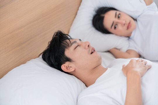 Couple in bed with one partner snoring while the other looks concerned during early morning hours