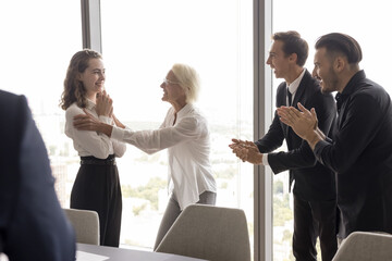 Moment of triumph. Smiling mature female ceo boss leader praise young girl manager employee before laughing applauding teammates recognize personal achievement acknowledge contribution in team success