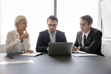 Teamwork and problem solving. Thoughtful businesspeople group teammates of diverse age engaged in business process analyze electronic documents develop strategy collaborate on report using notebook