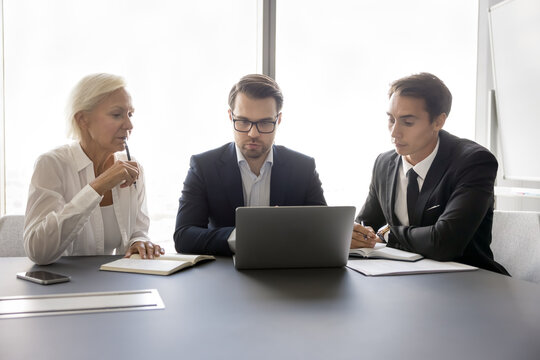 Teamwork and problem solving. Thoughtful businesspeople group teammates of diverse age engaged in business process analyze electronic documents develop strategy collaborate on report using notebook - Powered by Adobe