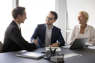 Welcoming new talent. Two diverse gender age corporate hr managers recruit young male applicant candidate for vacant position to office team confirm successful placement employment with handshaking