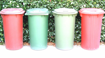 Four Plastic Recycling Bins in Red and Green Against a Green Hedge