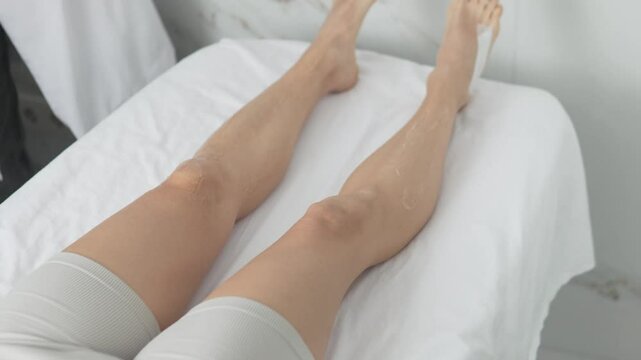 The cosmetologist applies a transparent gel to the client's lower leg before the laser hair removal procedure