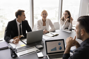 Data driven discussion. Diverse age business team professional managers executives work talk negotiate at conference desk brainstorm solution strategy based on statistic information on notebook screen