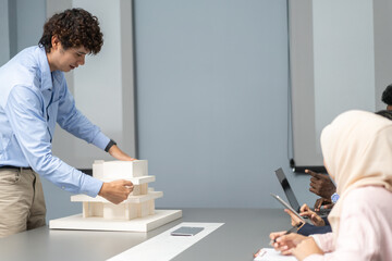 Architects engineers collaborating on building design project in modern office, diverse team of professionals female muslim architect and male engineers discussing architectural model of structure