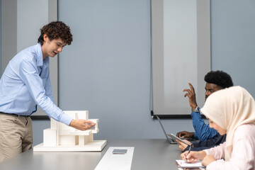Architects engineers collaborating on building design project in modern office, diverse team of professionals female muslim architect and male engineers discussing architectural model of structure