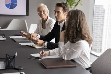 Creative problem solving. Young man manager in formal suit speak on team meeting with diverse office workers colleagues at boardroom table share fresh idea on brainstorm offer innovative business plan