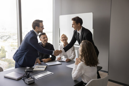 Positive interaction. Happy millennial business partners shaking hands on team boardroom meeting satisfied with successful collaboration express respect support agreement with offer idea making deal