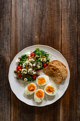 Delicious breakfast - boiled eggs with vegetables and feta cheese served on wooden table
