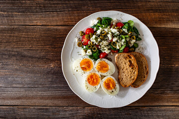 Delicious breakfast - boiled eggs with vegetables and feta cheese served on wooden table
