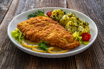 Breaded fried pork chop with fresh vegetable salad and potatoes on wooden table
