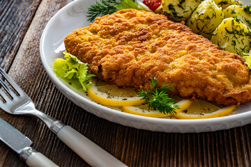 Breaded fried pork chop with fresh vegetable salad and potatoes on wooden table

