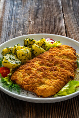 Breaded fried pork chop with fresh vegetable salad and potatoes on wooden table
