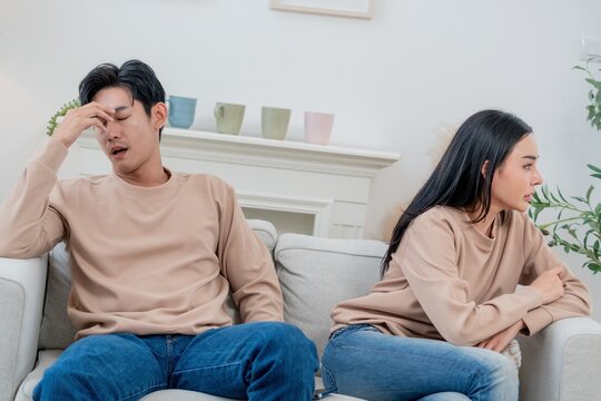 Couple sits apart in tense silence as frustration builds during a disagreement at home in the afternoon