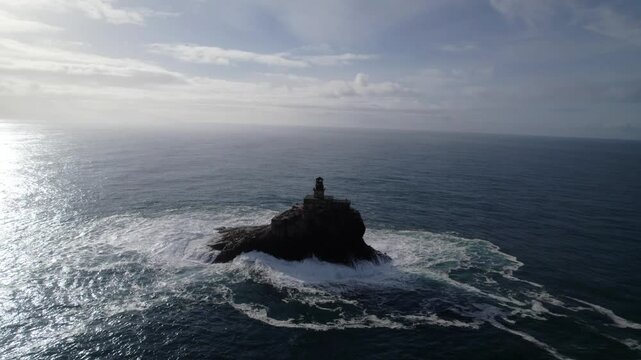 Aerial: Tillamook Rock Light lighthouse with waves crashing during the day in North Pacific Ocean, northern Oregon Coast, USA, establishing drone shot