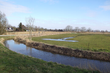 Obraz premium Pasture landscape in North Holland. Ditch, meadows with water puddles after rain. Cycle path in the distance. Village of Bergen. Netherlands, February