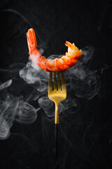Hot grilled shrimp on a fork. Seafood on a black stone background.