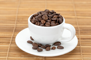 A white ceramic cup filled with roasted coffee beans gives off a rich aroma.