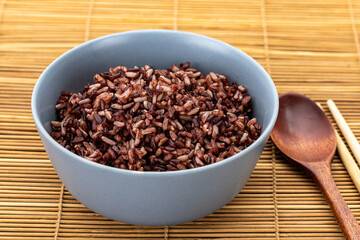 Healthy cooked brown rice mixed with riceberry in a grey ceramic bowl with a wooden spoon and bamboo chopsticks on the side.