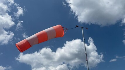 video of a wind sleeve to signal wind direction and intensity positioned at a parachute airfield, isolated against a blue sky with white clouds
