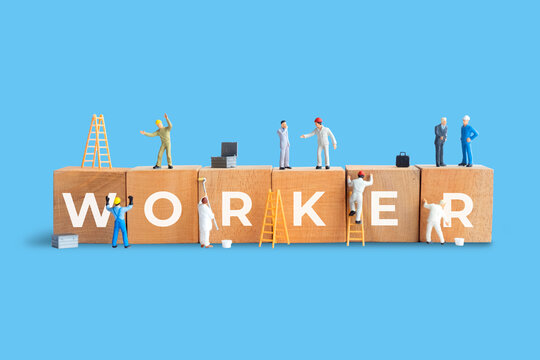 Wooden block with the word WORKER written on it with miniature people around it. Labour day and mayday concept 
