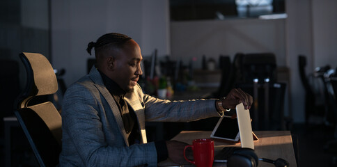 Young African-American IT manager, programmer or web developer closing his laptop in a dimly lit office. Concept of late work, business decision, technology, and productivity