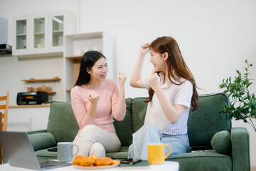 Two women enjoy remote work in a cozy living room, using a laptop while sipping coffee and chatting.
