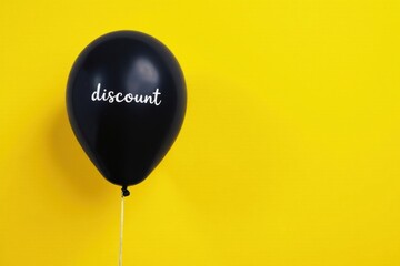 Obraz premium A single black balloon against a vibrant yellow backdrop, featuring the word discount, symbolizes a celebratory sale or promotional event.